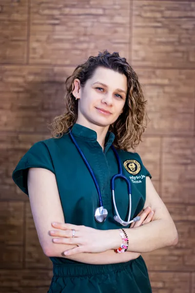 Veterinarijos gydytoja Ilona žalioje uniformoje prie medinės sienos
