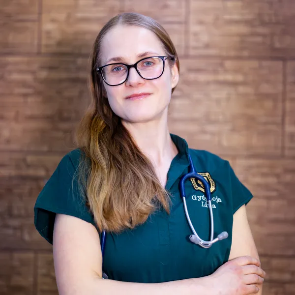 Veterinarijos gydytoja Lina su akiniais ir stetoskopu prie medinės sienos