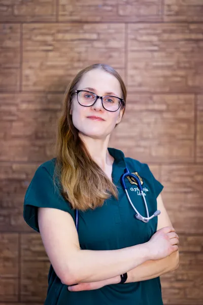 Veterinarijos gydytoja Lina žalioje uniformoje prie medinės sienos
